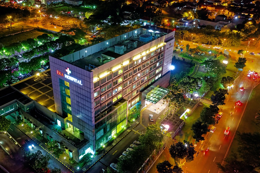 Outside shot of a well-lit hospital at night with a neon sign for EKA Hospital.
