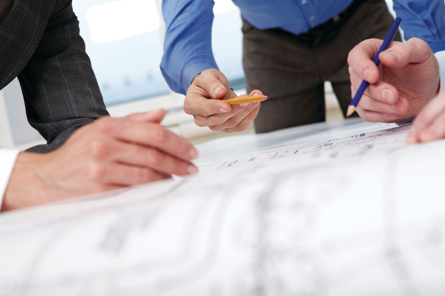 Design drawing close-up with three people working on them.