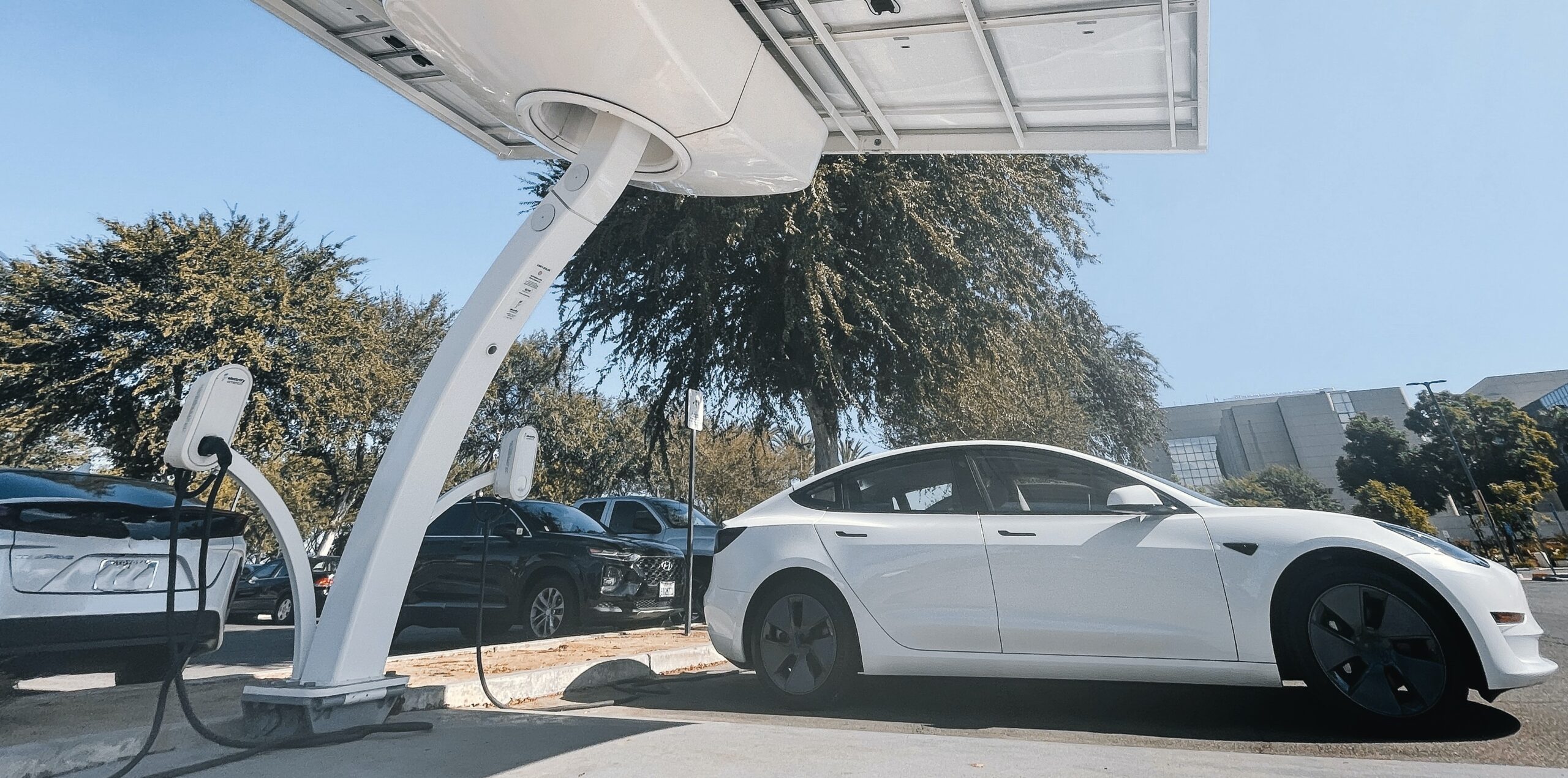 Two electronic vehicles plugged into a white solar powered EV charging station.